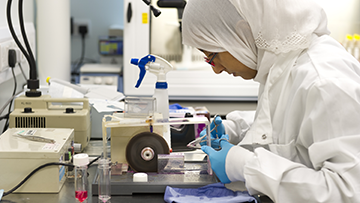 Woman wearing a labcoat, hijab and gloves doing an experiment
